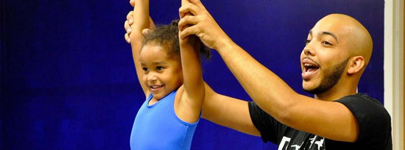 Black male alumnus opened his own dance studio in Charlotte, pictured with young dance student helping with position