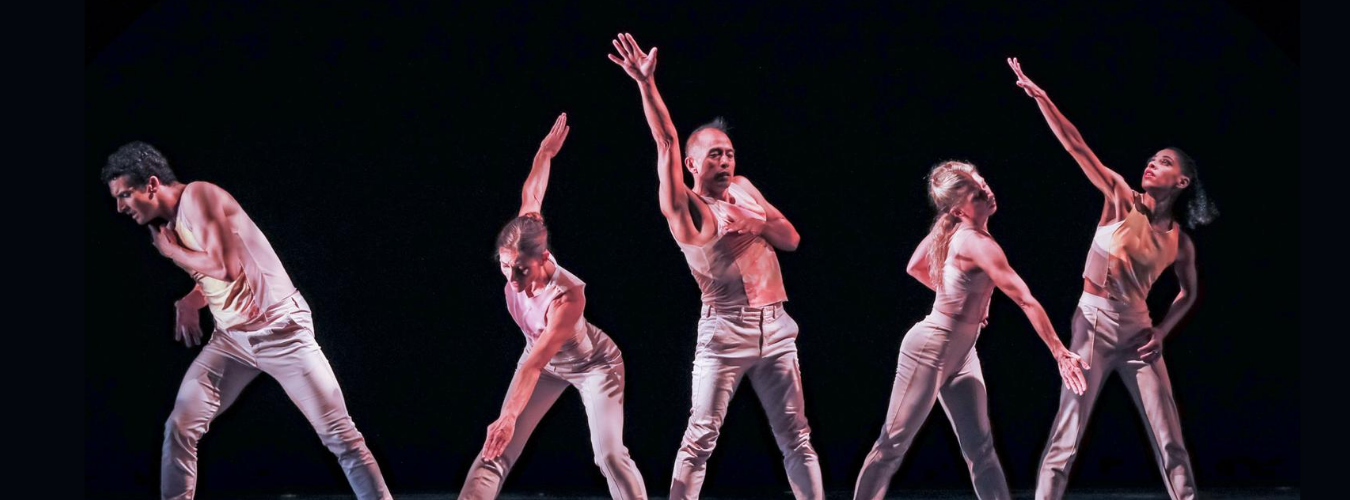 Five adult dancers in a line with a black background reaching different directions